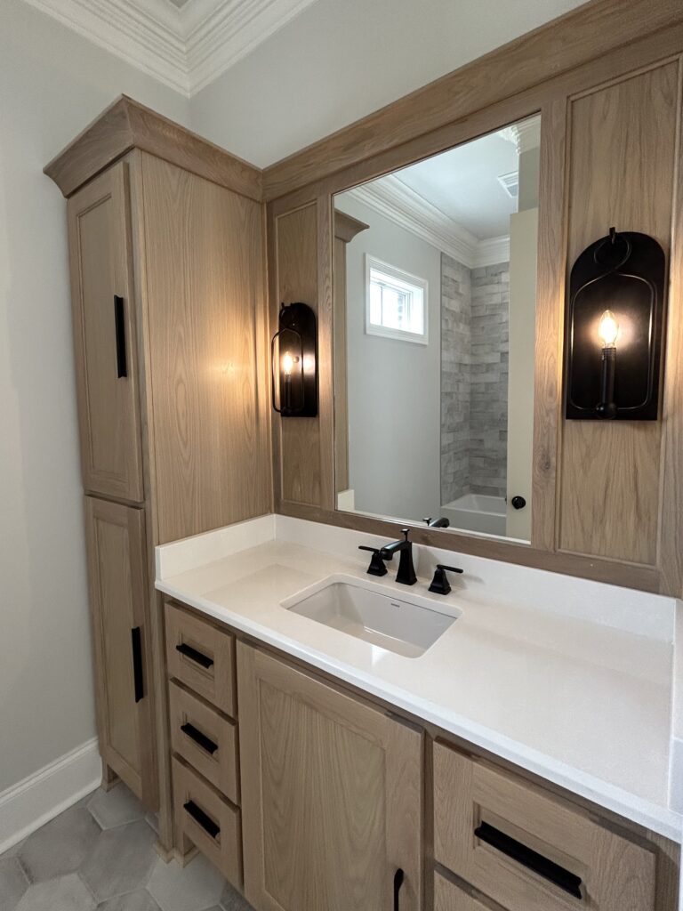 mirror over white bathroom sink surrounded by natural wood cabinets